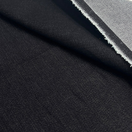 A close-up of black fabric with a visible woven texture and a folded edge showing a lighter gray underside.