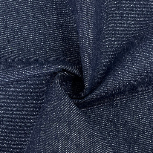 A close-up of dark indigo denim fabric with a textured twill weave, shown with a central swirl to highlight the material's drape and texture.