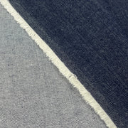 Close-up of a fabric material with a diagonal split between dark indigo blue and light gray, finished with a raw frayed edge.