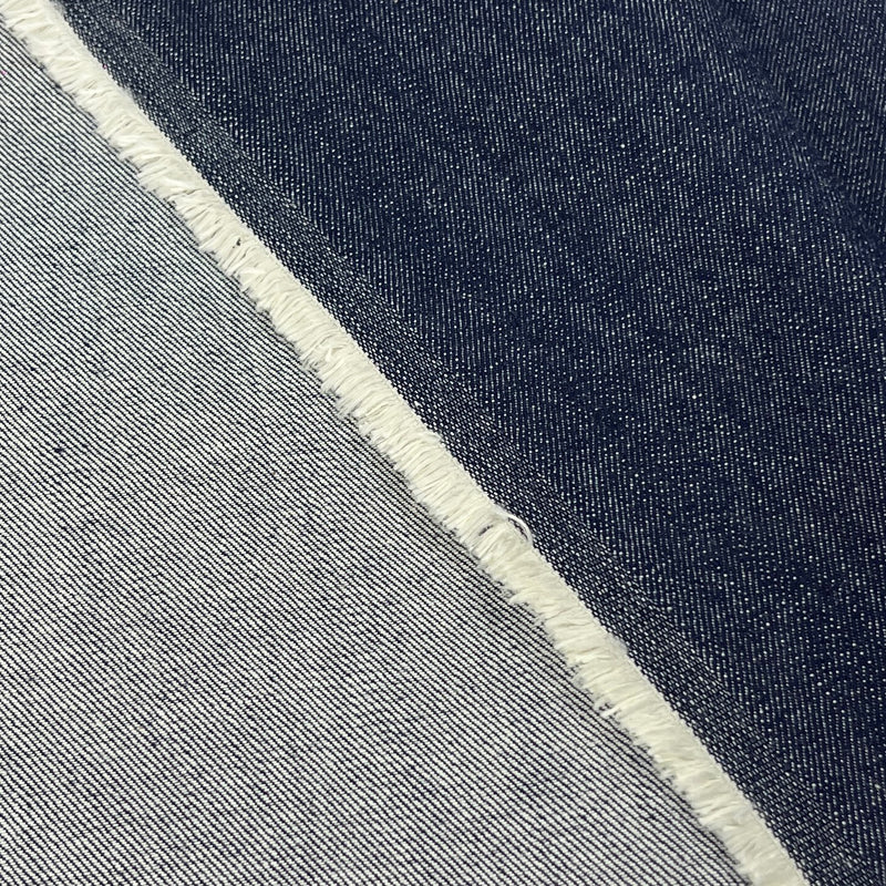 Close-up of a fabric material with a diagonal split between dark indigo blue and light gray, finished with a raw frayed edge.