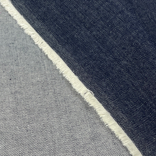 Close-up of a fabric material with a diagonal split between dark indigo blue and light gray, finished with a raw frayed edge.