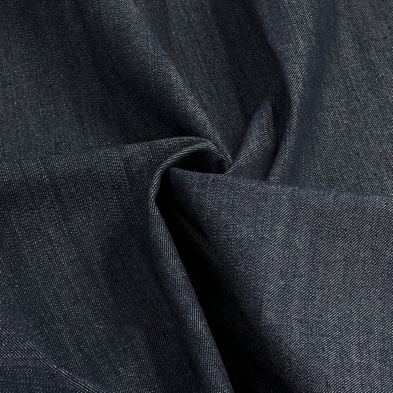 A close-up of dark indigo denim fabric with a textured twill weave, shown with soft folds and shadows.
