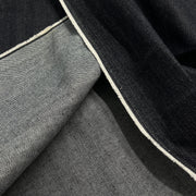 Close-up of folded dark indigo and medium gray denim fabric with a visible white stitched edge.