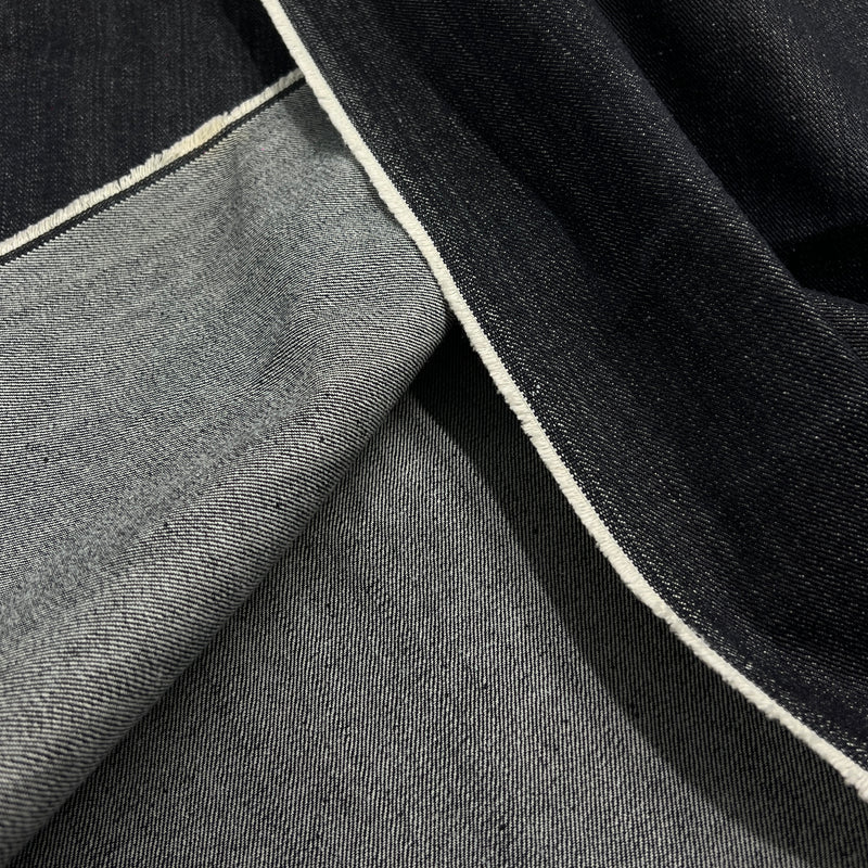 Close-up of folded dark indigo and medium gray denim fabric with a visible white stitched edge.