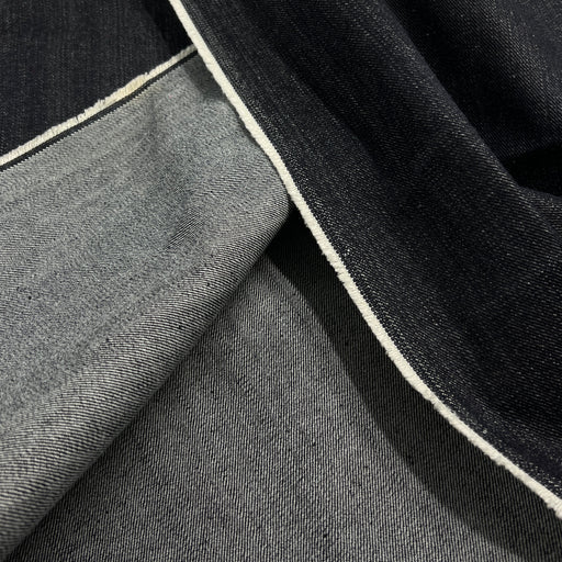 Close-up of folded dark indigo and medium gray denim fabric with a visible white stitched edge.