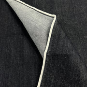 A close-up of dark indigo denim fabric with a folded corner revealing a light gray underside and a white stitched edge.