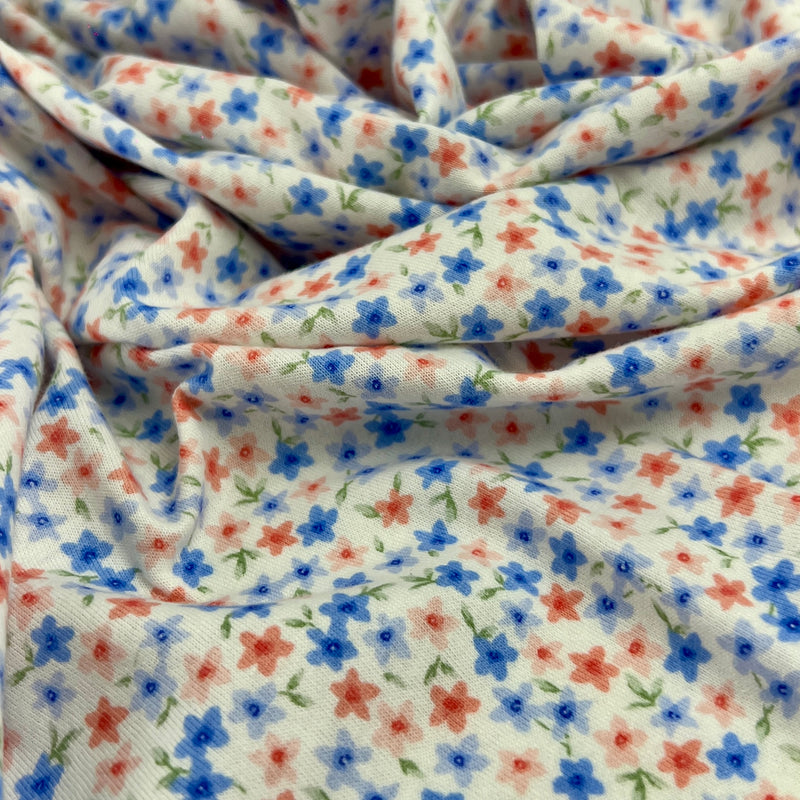 A close-up of draped fabric with a small-scale floral print featuring blue and red flowers with green stems on a white background.
