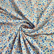 A close-up of draped fabric with a small-scale floral print, featuring blue and red flowers with green stems on a white background, arranged in a spiral drape.