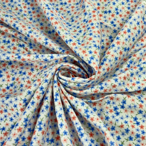 A close-up of draped fabric with a small-scale floral print, featuring blue and red flowers with green stems on a white background, arranged in a spiral drape.