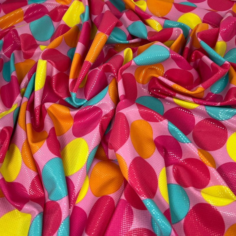 A close-up of draped fabric with a bright pink base and large overlapping polka dots in yellow, orange, teal, and magenta.