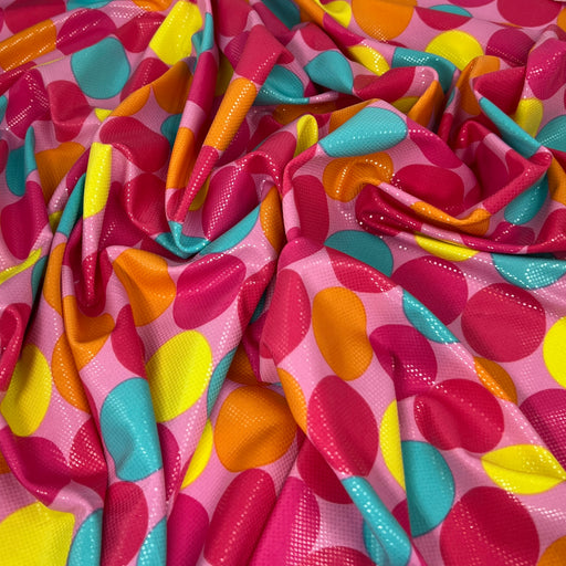 A close-up of draped fabric with a bright pink base and large overlapping polka dots in yellow, orange, teal, and magenta.