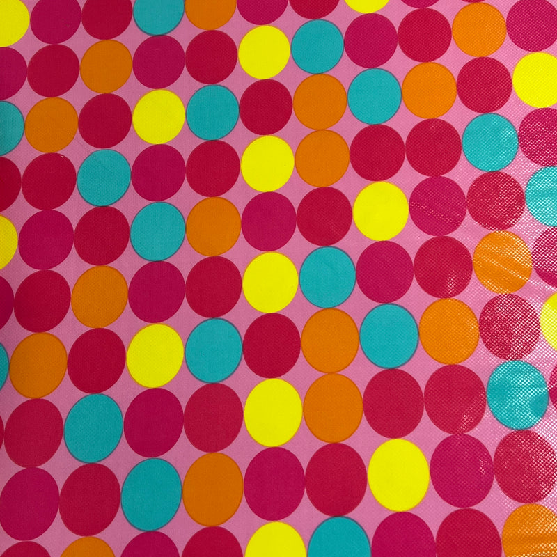 A close-up of a pink fabric or material covered in a repeating pattern of overlapping circles in red, yellow, orange, and turquoise.