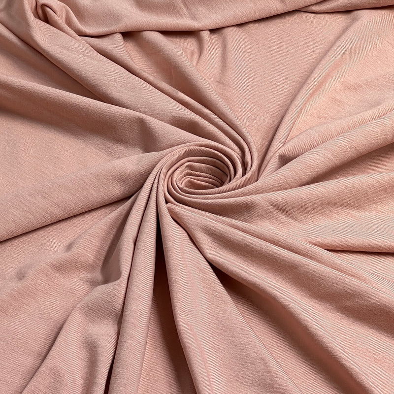 A close-up of draped dusty pink fabric arranged in a spiral pattern, showing the soft texture and color of the material.
