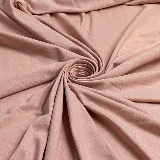 A close-up of draped dusty pink fabric arranged in a spiral pattern, showing the soft texture and color of the material.