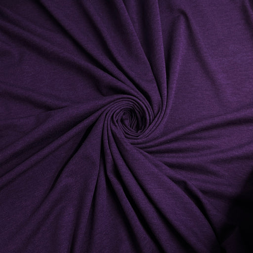 A close-up of draped purple fabric arranged in a spiral pattern, showing its texture and color.