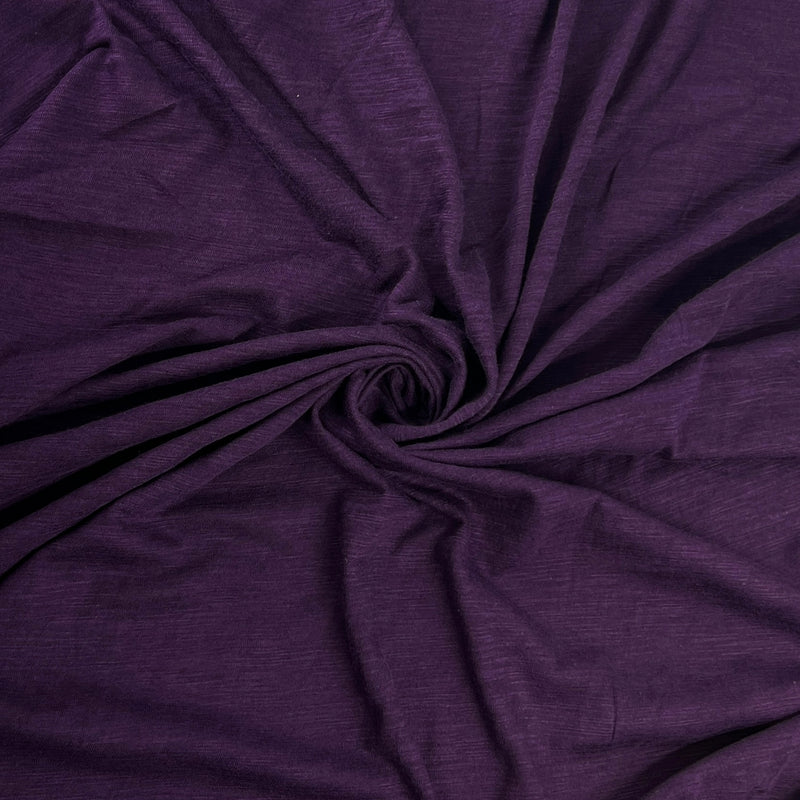 A close-up of draped purple fabric arranged in a spiral swirl, showing the material texture and color.