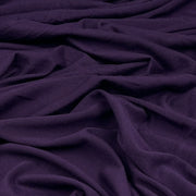 A close-up of draped dark purple fabric with soft folds and a smooth texture.