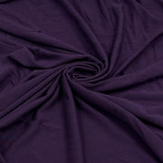 A close-up of draped dark purple fabric arranged in a spiral pattern, showing its soft texture and folds.