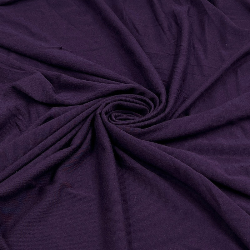 A close-up of draped dark purple fabric arranged in a spiral pattern, showing its soft texture and folds.