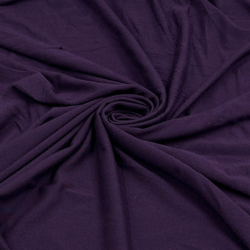 A close-up of draped dark purple fabric arranged in a spiral pattern, showing its soft texture and folds.