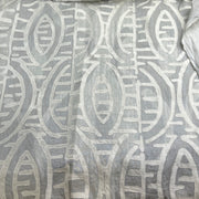 A close-up of a light gray fabric with a raised, textured off-white geometric pattern.