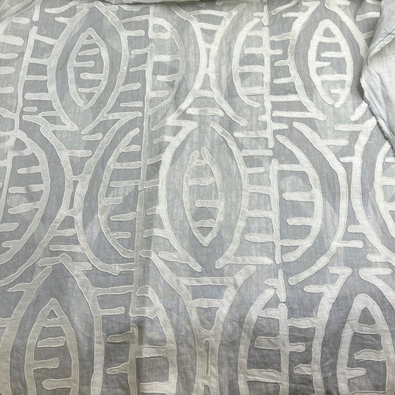 A close-up of a light gray fabric with a raised, textured off-white geometric pattern.