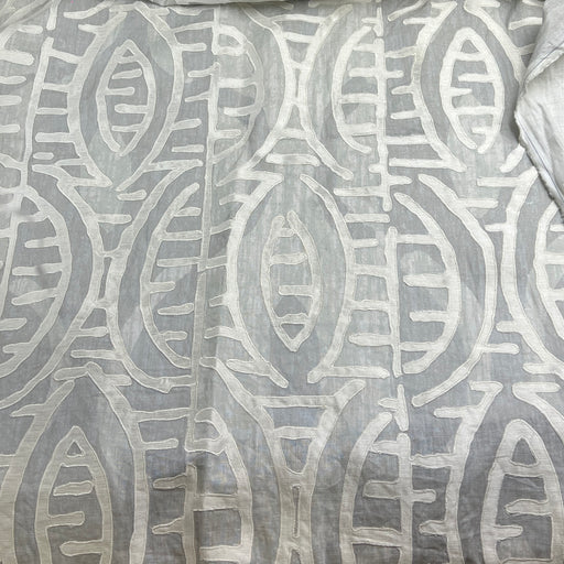 A close-up of a light gray fabric with a raised, textured off-white geometric pattern.