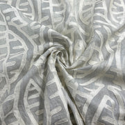 A close-up of draped fabric with an abstract leaf-like pattern in light gray and off-white, arranged in a spiral fold.