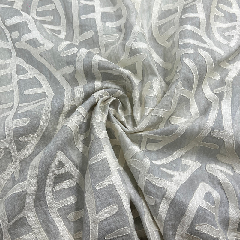 A close-up of draped fabric with an abstract leaf-like pattern in light gray and off-white, arranged in a spiral fold.