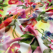 A close-up of draped fabric featuring a vibrant watercolor floral print with pink, red, yellow, blue, and green tones on a white base.