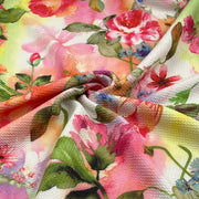 A close-up of a textured fabric with a vibrant watercolor floral print featuring pink, red, yellow, and green flowers on a white background.