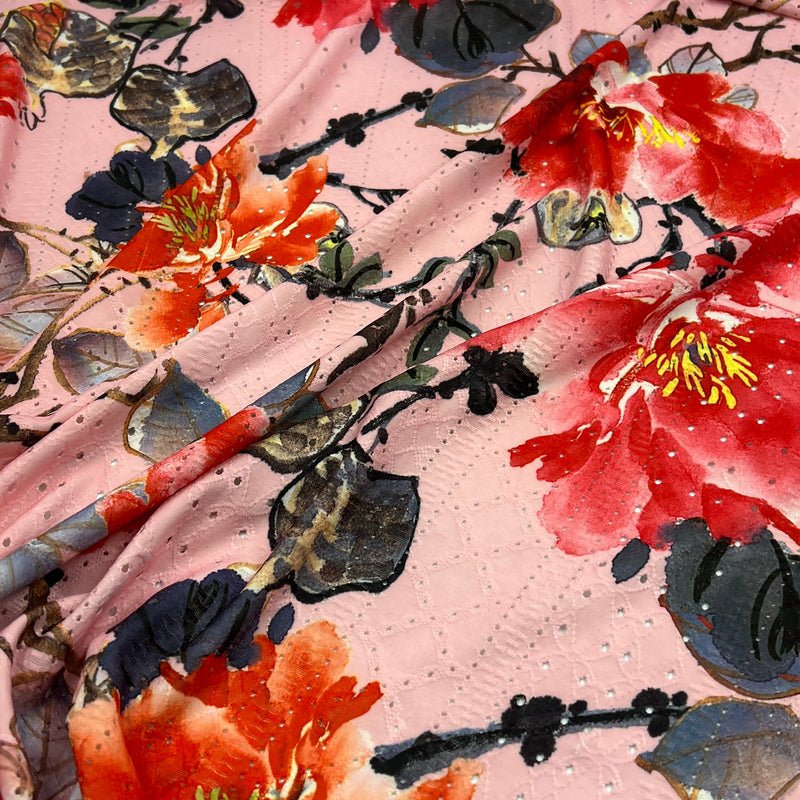 A close-up of a draped pink fabric featuring a vibrant watercolor floral print with red, orange, and dark gray flowers.