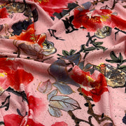 Pink floral fabric with a textured, perforated surface, featuring large red and orange flowers with blue-gray leaves and gold accents.