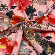A close-up of a pink floral fabric with a textured, dotted jacquard-like weave. The design features large watercolor-style red, orange, black, and gray flowers with green leaves, arranged in a spiral drape.