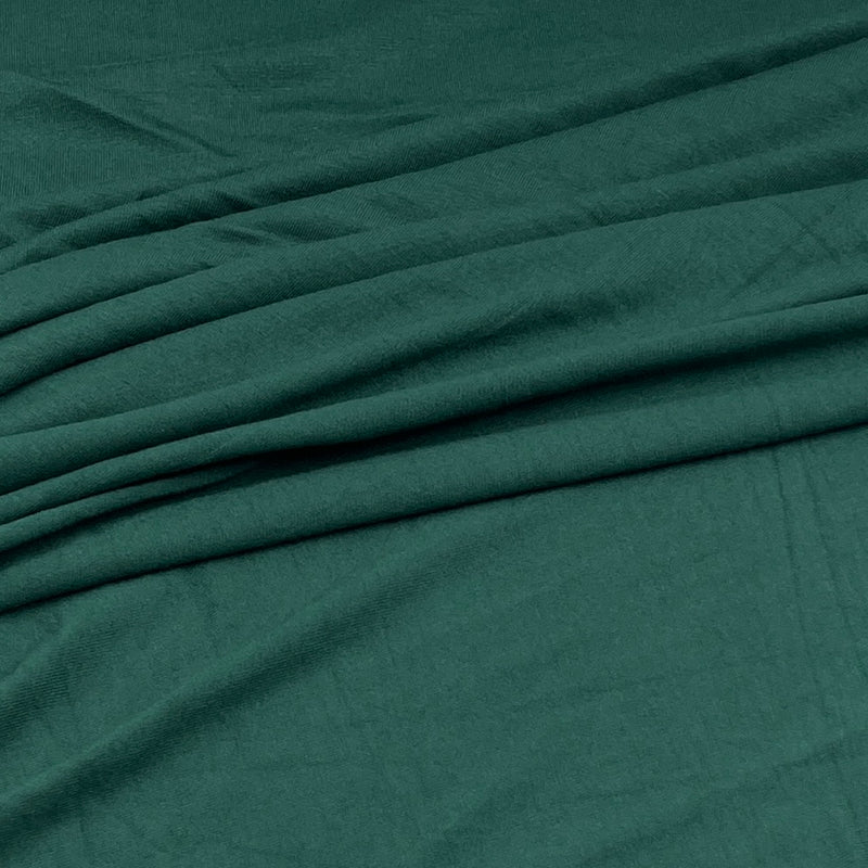 A close-up of draped dark teal green fabric with soft folds and a smooth texture.