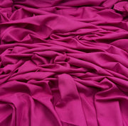 Bright fuchsia rayon challis fabric draped into a pile showing off smooth silky texture. 