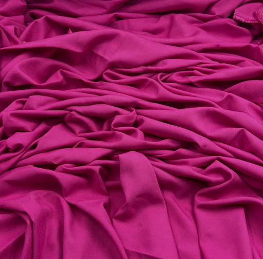 Bright fuchsia rayon challis fabric draped into a pile showing off smooth silky texture. 