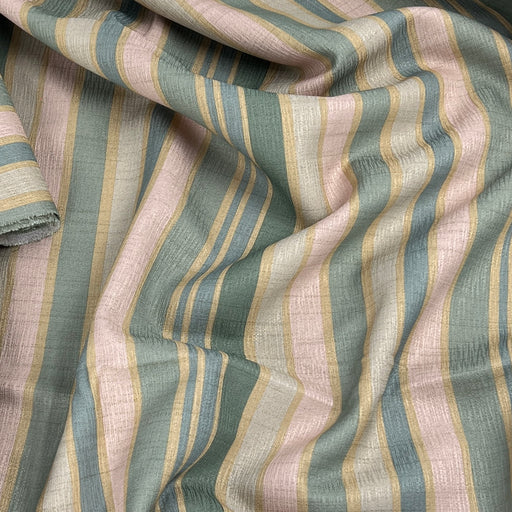 A close-up of draped striped fabric with vertical bands in muted sage green, dusty pink, soft blue, and tan on a white base.