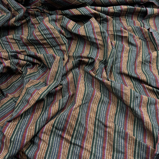 A close-up of draped striped fabric with vertical bands in brown, beige, muted red, and dark gray, featuring small white dotted accents.