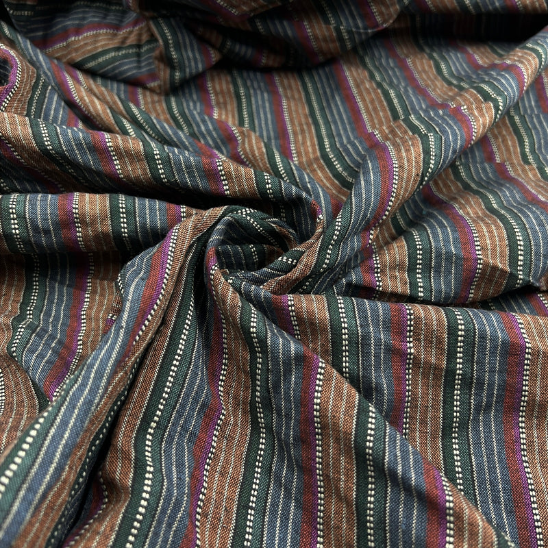 A close-up of a striped fabric with vertical bands of brown, navy, teal, and burgundy, accented by thin white dotted lines and woven texture.