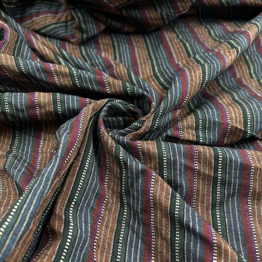 A close-up of a striped fabric with vertical bands of brown, navy, teal, and burgundy, accented by thin white dotted lines and woven texture.