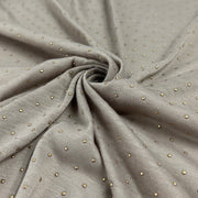 A close-up of draped taupe-gray fabric with a fine woven texture and small scattered metallic gold dot embellishments, arranged in a central swirl.