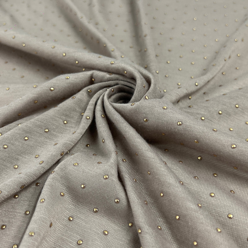 A close-up of draped taupe-gray fabric with a fine woven texture and small scattered metallic gold dot embellishments, arranged in a central swirl.