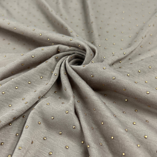 A close-up of draped taupe-gray fabric with a fine woven texture and small scattered metallic gold dot embellishments, arranged in a central swirl.