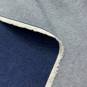 A close-up of fabric showing two colorways: a light gray woven texture with a white frayed edge, and a dark navy blue woven texture. The fabrics are layered to show both sides of the material.