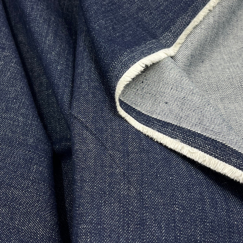 Close-up of dark indigo denim fabric with a folded corner showing the lighter inner side and a white frayed edge.