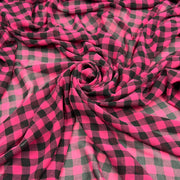 Bright pink and black buffalo plaid fabric draped in a spiral pattern, showing its soft texture and checkered design.