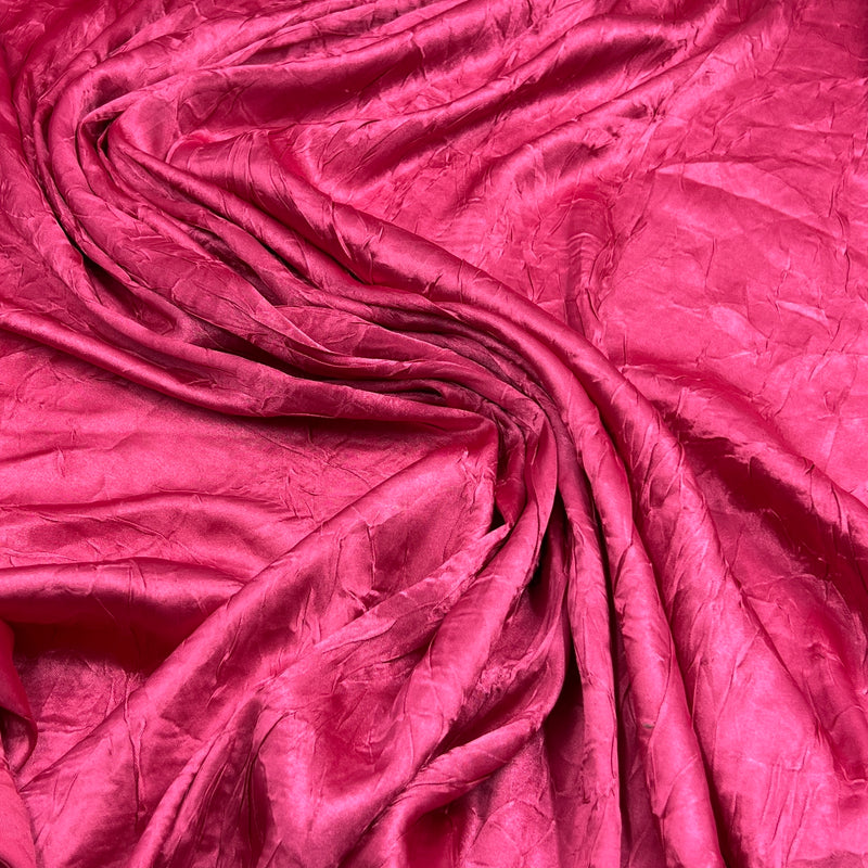 A close-up of draped magenta pink crinkled fabric, showing its texture and sheen.