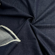 A close-up of dark navy blue fabric with a textured weave, draped in soft folds. A folded section on the left reveals a lighter gray inner layer with a dark navy stitched edge.