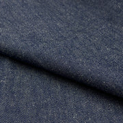 A close-up of dark indigo denim fabric with a diagonal fold showing the textured twill weave.
